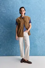 Chaleco de algodón color beige, de calce relajado, con cuello clásico, hombros amplios, cierre frontal con broches metálicos y bolsillos delanteros con solapa.