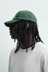 Gorra de siete paneles verde oscuro con efecto lavado, visera curva y bordado frontal en tono amarillo con la inscripción 'Bahia Montego'. Cuenta con ajuste posterior.