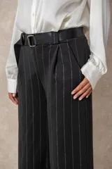 Pantalón de corte ancho y tiro alto, confeccionado en tejido azul marino con finas rayas verticales de hilo de lurex plateado. Presenta cintura con pasacintos y se incluye un cinturón negro con hebilla metálica.