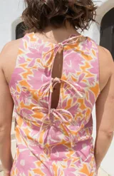 Top sin mangas con cuello redondo, confeccionado en lino con estampado floral en tonos rosados y naranjas. Presenta un diseño con cierre de tres lazos en la espalda.