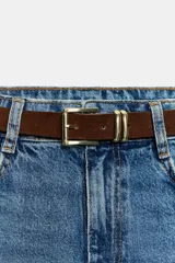 Jeans blancos wide leg cropped de tiro alto, con diseño de cinco bolsillos y pernera ancha y corta. Incluye un cinturón fino de color marrón oscuro con hebilla metálica y cuenta con cierre frontal de cremallera y botón metálico.