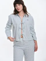 Camisa de dormir de popelina de algodón, con estampado de rayas verticales y pequeños motivos geométricos. Presenta cuello camisero, mangas largas y cierre frontal mediante lazos ajustables.