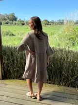 Vestido corto de lino color beige claro, con cuello mao, escote con botones de nácar, mangas tres cuartos con volados y ruedo con volado.