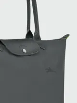 Bolso tote Longchamp modelo Le Pliage Green L, color marrón chocolate, confeccionado en lona de nylon reciclado con detalles en cuero ruso color marrón oscuro. Cuenta con cierre de cremallera y botón a presión, asas cortas para llevar al hombro y es plegable para facilitar su almacenamiento.