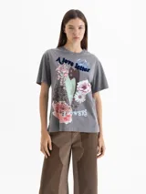 Remera gris con efecto lavado, de corte holgado y cuello redondo. Presenta una estampa frontal con motivos florales, un corazón central y la inscripción 'A love letter to winter flowers'. Cuenta con tajos laterales en el ruedo.