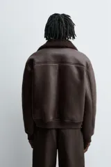 Cazadora oversize de efecto piel color negro, con interior y cuello solapa de pelo sintético gris a contraste. Cuenta con bolsillos de vivo en la cadera, acabados en rib elástico y cierre frontal con cremallera.