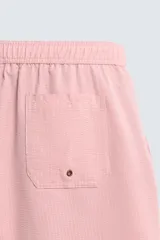 Bañador largo de hombre color rosa pálido con textura seersucker. Presenta cintura elástica ajustable con cordón blanco, bolsillos laterales y un bolsillo trasero de plastrón.