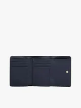 Billetera plegable en tres partes (trifold) de color beige claro, con acabado liso y cierre de solapa. Presenta una insignia metálica dorada con el monograma TH en el frente y un bolsillo exterior con cierre de cremallera.