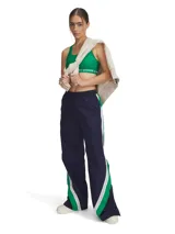 Pantalón deportivo de corte holgado y pierna ancha, confeccionado en tejido de nailon con textura arrugada. Presenta un diseño en color azul marino con paneles laterales en verde y blanco, cintura elástica y botones a presión en los laterales de las piernas.