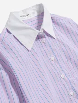 Camisa de manga larga con cuello y puños blancos contrastantes. El cuerpo de la camisa es de color crema con finas rayas verticales azules y tiene un corte crop.