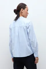 Camisa de manga larga a rayas celestes y blancas, con cuello mao y volados verticales en el frente.