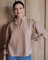 Blusa de algodón con estampado de rayas verticales en color tostado y blanco. Presenta cuello mao con volados, escote en V y mangas largas abullonadas con puños acampanados.