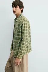 Camisa de corte relajado confeccionada en tejido de algodón con estampado de cuadros en tonos verdes y beige. Presenta cuello solapa, cierre frontal con botones a presión, bolsillos plastrón en el pecho y mangas largas con puños abotonados.