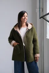 Tapado de paño color verde oliva con interior y detalles en beige. Presenta capucha amplia, cierre frontal, bolsillos laterales y mangas con puños vueltos que dejan ver el contraste de color.