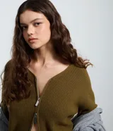 Cardigan de punto color verde militar, con cuello en V, mangas largas abullonadas y cierre frontal de cremallera bilateral.