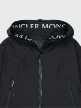 Chaqueta negra con capucha y cierre frontal con cremallera. Logotipo de Moncler en el borde de la capucha.