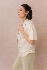 Chaleco de jean color crudo, con calce relajado y largo a la cintura. Cuenta con cuello camisero, cierre frontal con botones metálicos y bolsillos delanteros con tapa.