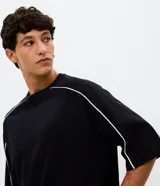 Remera masculina de corte boxy, color negro, con cuello redondo y mangas cortas amplias. Presenta detalles de vivos blancos en contraste a lo largo de las costuras de las mangas y hombros.