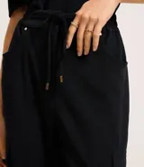 Pantalón negro de crepé con corte carrot, cintura alta con elástico en la parte trasera y lazo en la delantera, bolsillos delanteros con detalle metalizado y bolsillos cargo laterales.