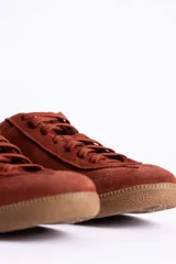 Zapatillas de gamuza color marrón con suela de goma color caramelo. Presentan cordones al tono y un detalle decorativo de pañuelo estampado atado en los laterales con esferas metálicas doradas.