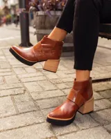 Botineta de cuero negro con diseño combinado en cuero charolado, plataforma y taco cuadrado de madera clara. Presenta cierre lateral y puntera redondeada.