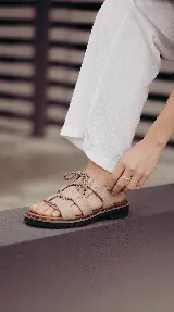 Sandalia de cuero color visón con tiras anchas entrelazadas, cordones ajustables en el empeine, suela dentada y base de goma.