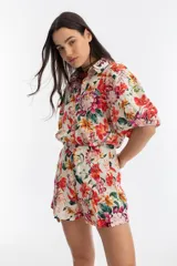 Short de lino color blanco con estampado floral en tonos rojos, amarillos, verdes y rosas. Tiene cintura alta con tablas, bolsillos laterales y cierre frontal con gancho metálico.