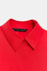 Camisa roja de cuello solapa, con mangas cortas abullonadas tipo globo y cierre frontal con botones ocultos.