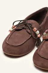 Mocasín estilo náutico de gamuza marrón, con cordones de cuero, borla decorativa y cuentas de colores en el empeine.