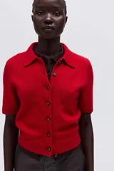 Saco de punto suave color rojo, con cuello camisero, cierre frontal de botones y mangas cortas con terminaciones acanaladas.