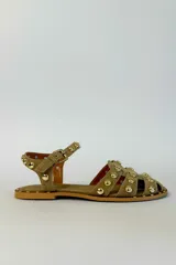 Sandalias planas de gamuza color tostado, con múltiples tiras decoradas con tachas metálicas doradas semiesféricas. Cuenta con una tira ajustable en el tobillo con hebilla metálica.