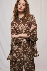 Camisa de silueta amplia y largo por debajo de la cadera, confeccionada en tela liviana con estampado floral en tonos marrón y tostado. Presenta cuello clásico, cierre frontal con botones y mangas tres cuartos.