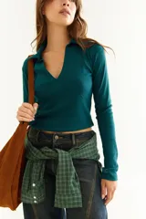 Top de manga larga color verde petróleo, con cuello polo y escote en V pronunciado. Presenta recortes diagonales en el frente y un pequeño bordado en el puño.