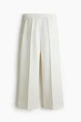 Pantalón de vestir blanco con cintura clásica, cierre con botón oculto y corchete. Presenta bolsillos al bies, bolsillo trasero decorativo y piernas amplias con pliegues marcados adelante y atrás.