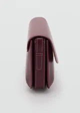 Bolso tipo bandolera de tamaño pequeño con acabado efecto piel en color bordó. Presenta una solapa frontal con cierre metálico a presión, costuras visibles en contraste y una correa larga ajustable con herrajes dorados.