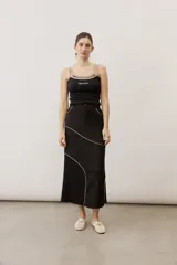 Pollera midi de corte recto, color negro, con costuras curvas decorativas en tono tostado y un panel lateral de encaje.