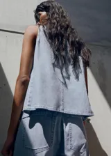 Top sin mangas estilo chaleco confeccionado en tejido de algodón tipo denim. Presenta un diseño recto, cuello redondo y cierre frontal con botones.