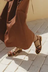 Sandalia plana de cuero blanco con diseño de tiras trenzadas en la parte delantera. Cuenta con una tira ajustable al tobillo con hebilla metálica y suela plana de color negro.