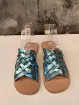 Sandalias chatas con tiras de cuero metálico color celeste trenzadas.