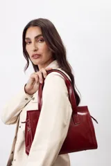 Cartera mini tote de cuero vacuno color bordó, con acabado charol, doble asa de mano y estructura rígida.