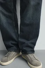 Zapatilla deportiva de hombre confeccionada en piel con acabado de serraje. Presenta un diseño minimalista con cordones al tono y un detalle en contraste de color en la pieza del talón. Cuenta con una suela de goma con volumen.