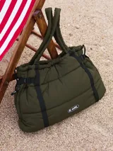 Bolso tipo tote acolchado de color verde militar, con cierre lateral y correas ajustables. Cuenta con el logo de la marca en la parte frontal y diseño abullonado.