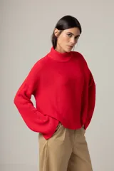 Sweater de tejido de punto en color rojo, con cuello alto y mangas largas acampanadas. Presenta un diseño de corte recto y holgado.