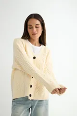 Cardigan de punto con diseño de trenzas, color beige, con escote en V, cierre frontal de botones negros y mangas largas con puños acanalados.