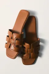 Sandalias planas de cuero marrón, con punta cuadrada y tiras superiores entrelazadas con diseño geométrico y acolchado.
