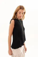 Blusa negra sin mangas con textura arrugada, cuello redondo y detalle de volados en los hombros. Presenta un corte asimétrico en el ruedo.