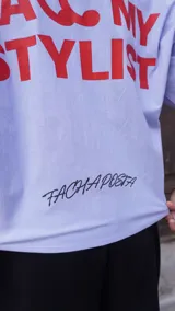 Camisa de corte boxy fit color celeste, con mangas cortas y cuello tipo polo. Presenta un estampado frontal en color rojo con la frase 'CALL MY STYLIST' y un detalle bordado en color negro con la firma 'FACHAPOSTA'.