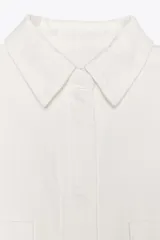 Sobrecamisa blanca de algodón con cuello solapa, manga larga y dos bolsillos de plastrón en el pecho. Cierre frontal con botones ocultos por solapa.