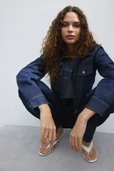 Campera cropped de denim de algodón rígido, color azul, con cuello, cierre frontal de botones y hombros caídos. Cuenta con bolsillos superiores con solapa y botón, puños abotonados y dobladillo deshilachado.