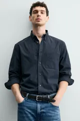 Camisa de corte regular fit confeccionada en tejido de algodón. Presenta cuello con solapa abotonada, cierre frontal con botones, manga larga con puños abotonados y un bolsillo plastrón en el pecho.